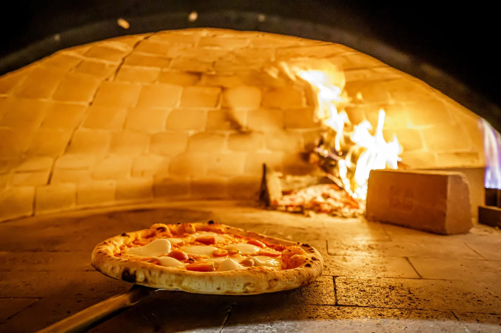The wood-fired oven at VIVA, flames inside the brick dome with a pizza on the peel.